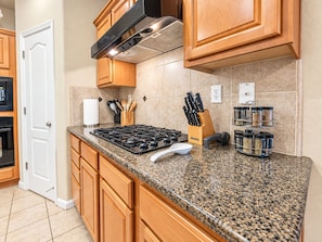 A kitchen with granite countertops, wooden cabinets, a stainless steel range hood, and a spice rack.