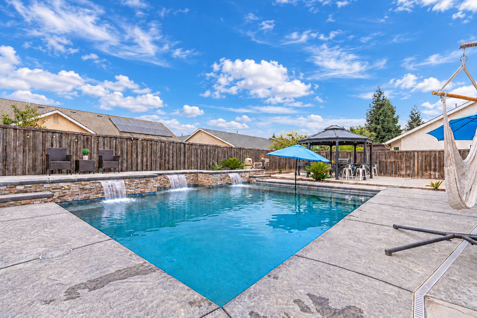 Un jardin avec une piscine, une clôture en bois, du mobilier d’extérieur et un belvédère.