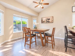 A dining area with a wooden table and chairs, a ceiling fan, and a window with a view of greenery.