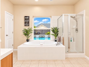 Um banheiro com uma banheira grande, chuveiro e janela com vista para uma casa e piscina.
