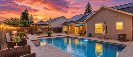 A backyard with a swimming pool, outdoor furniture, and a covered patio area.