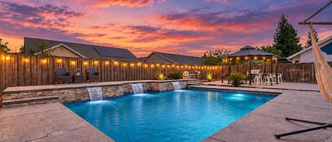 Un jardin avec une piscine, une clôture en bois, du mobilier d’extérieur et un belvédère.