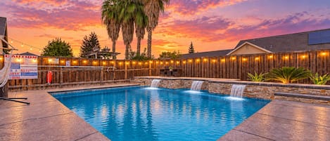 A swimming pool with a wooden deck and a wooden fence with string lights.