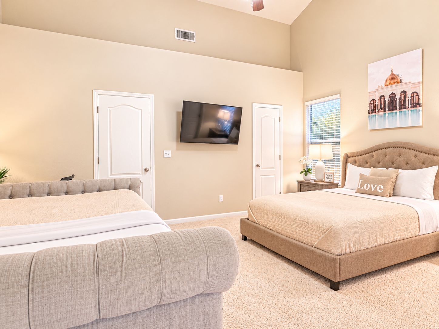A hotel room with two beds, a television, a window with blinds, and a painting on the wall.