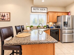 A kitchen with a granite countertop, stainless steel appliances, wooden cabinets, and a dining area with leather chairs. - Beautiful home W/Pool Close to National Parks. (Fresno)