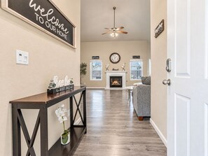 A hallway with a fireplace, a sofa, a clock, and a welcome sign. - Beautiful home W/Pool Close to National Parks. (Fresno)
