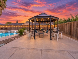 A covered outdoor patio with a pool, seating, and a wooden fence.