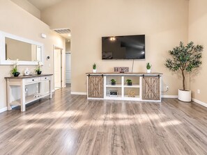 A modern interior with a wooden floor, a white console table, a flat-screen TV, and a potted plant. - Beautiful home W/Pool Close to National Parks. (Fresno)