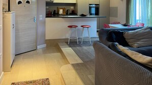 A modern kitchen with a central island, two bar stools, and a dining area with red chairs. - Lake View Apartment (Qarku i Tiranës)