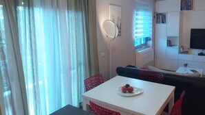 A modern living room with a white sofa, a dining table with a plate of fruit, a red chair, and a TV mounted on the wall. - Lake View Apartment (Qarku i Tiranës)