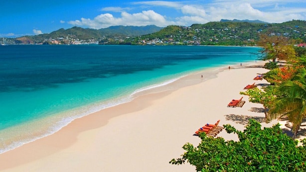 Una playa con agua turquesa cristalina, una orilla arenosa y sillas de playa rojas.