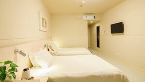 A hotel room with two beds, a bedside table with a lamp, a TV mounted on the wall, and a small plant on the left side. - Jinjiang Inn (Baotou Railway Station) (Baotou)