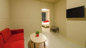 A hotel room with a red sofa, a small round table with a plant, a TV mounted on the wall, and a bed visible through an open door. - Jinjiang Inn (Baotou Railway Station) (Baotou)