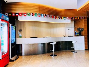 A reception area with a counter, two bar stools, a vending machine, and a wall with flags.