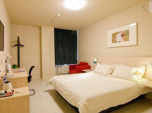 A hotel room with a bed, a desk with a chair, a red sofa, and a painting on the wall.