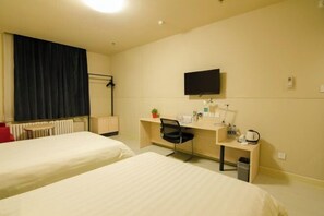 Habitación de hotel con dos camas, un escritorio con silla, televisor, radiador y un pequeño cubo de basura.