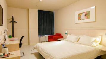 A hotel room with a bed, a desk with a chair, a red sofa, and a painting on the wall.
