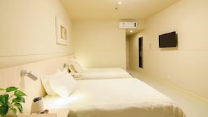 Une chambre d’hôtel avec deux lits, une table de chevet avec une lampe, un téléviseur fixé au mur et une petite plante sur le côté gauche.