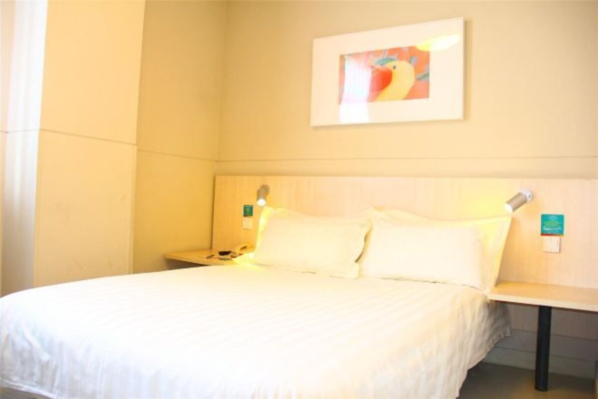 Una habitación de hotel con una cama, una mesita de noche, una lámpara de pared y un cuadro enmarcado.