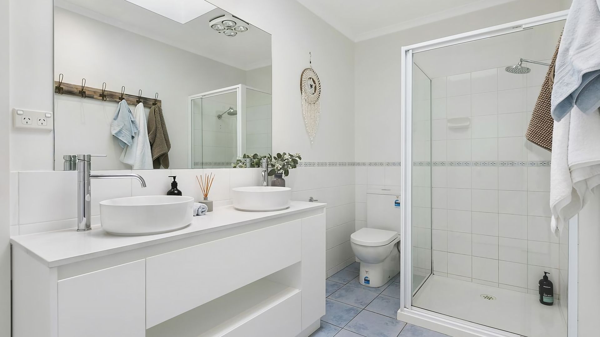 Een moderne badkamer met twee wastafels, een toilet en een douchecabine met glazen wanden.
