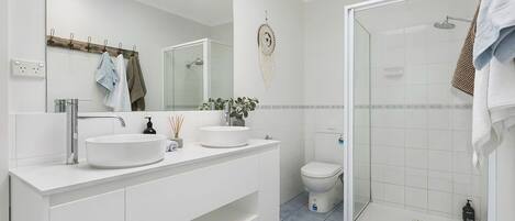 Een moderne badkamer met twee wastafels, een toilet en een douchecabine met glazen wanden.
