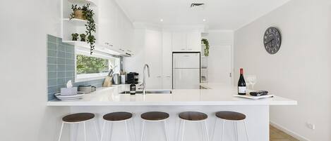 Une cuisine moderne avec des meubles blancs, un réfrigérateur encastré et un coin bar avec des tabourets.