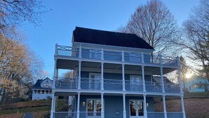 A multi-story building with a balcony on each floor, surrounded by trees and a grassy area. - Charming Victorian home (Groton)