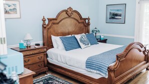 A bedroom with a wooden bed, a nightstand, a lamp, and a framed picture on the wall. - Charming Victorian home (Groton)