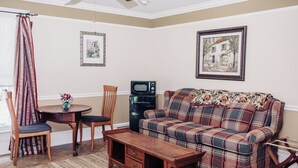 A living room with a plaid sofa, a wooden coffee table, a dining table with chairs, a microwave, and two framed pictures on the wall. - Charming Victorian home (Groton)