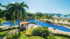 Ein Resort mit großem Schwimmbad, Palmen und Blick auf den Strand.