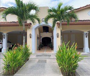 A building entrance with a covered walkway, palm trees, and potted plants.