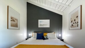 A neatly made bed with a white and yellow blanket, a single pillow with a blue and yellow design, and a framed picture above the bed. - Stylish Apt Near Disney and Airport (Santa Ana)