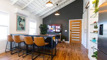 A modern kitchen with a wooden ceiling, a bar area with stools, a flat-screen TV, and a refrigerator.