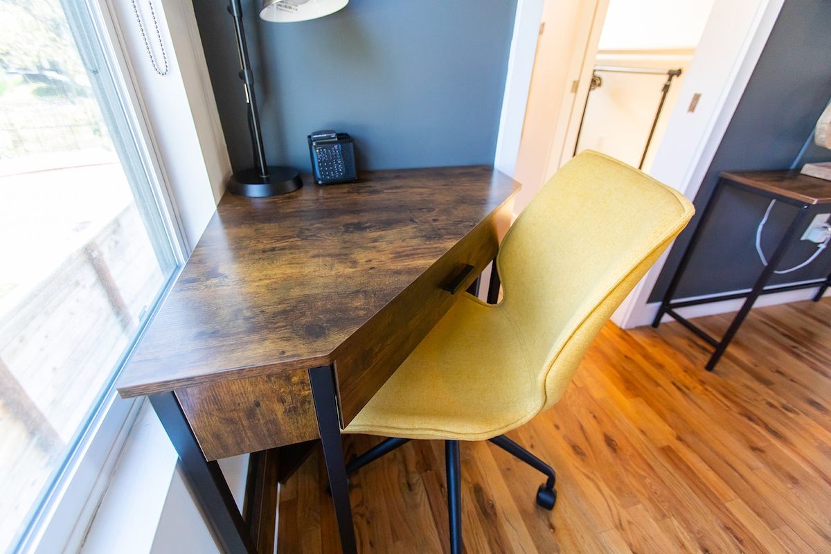 A wooden desk with a yellow chair in a room with wooden flooring and a window.
