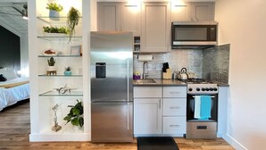 A compact kitchen with a stainless steel refrigerator, a microwave, and a gas stove. There are wooden cabinets and a tiled backsplash. - Stylish Apt Near Disney and Airport (Santa Ana)