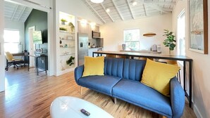 A modern living room with a blue sofa, yellow cushions, a white coffee table, and a kitchen in the background. - Stylish Apt Near Disney and Airport (Santa Ana)