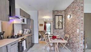 Una cocina moderna con microondas, estufa y lavamanos. Hay una zona de comedor con mesa y sillas. La cocina tiene una pared de ladrillo y una araña.