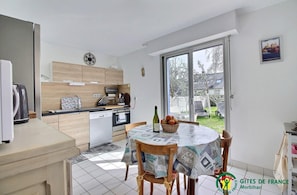 A compact kitchen with modern appliances, a dining area with a patterned tablecloth, and a view of the outdoors. - KER Malo - Etel - Gîte (ETEL)