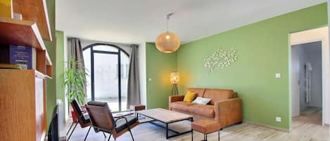 Una sala de estar moderna con un sofá, una mesa de centro y sillones. Hay una estantería, una lámpara y un elemento decorativo en la pared.