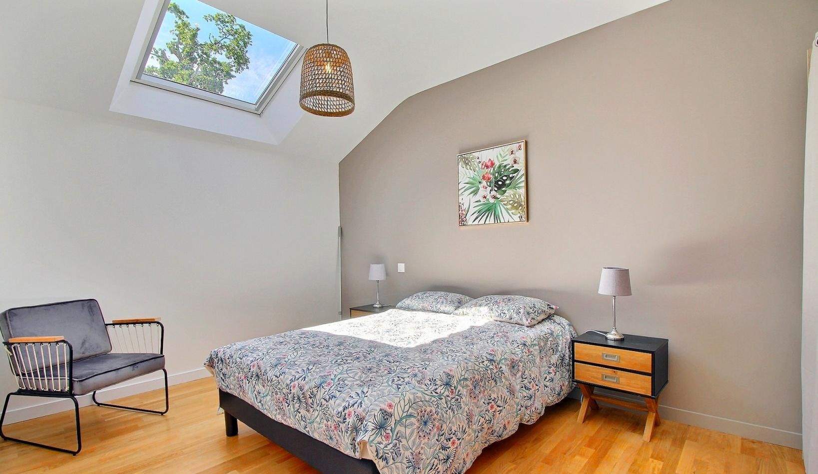 Un dormitorio con una cama, una silla, una mesita de noche, una lámpara, una ventana y una luz en el techo.