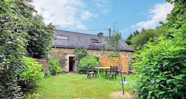 A stone building with a sloped roof, a wooden door, and a small garden with a table and chairs. - Hoëdic - SURZUR - Vacation Home (SURZUR)