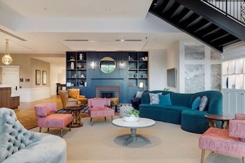 A modern hotel room with a large window, a white armchair, a floor lamp, and a small side table with magazines. at Canopy By Hilton Boston Downtown