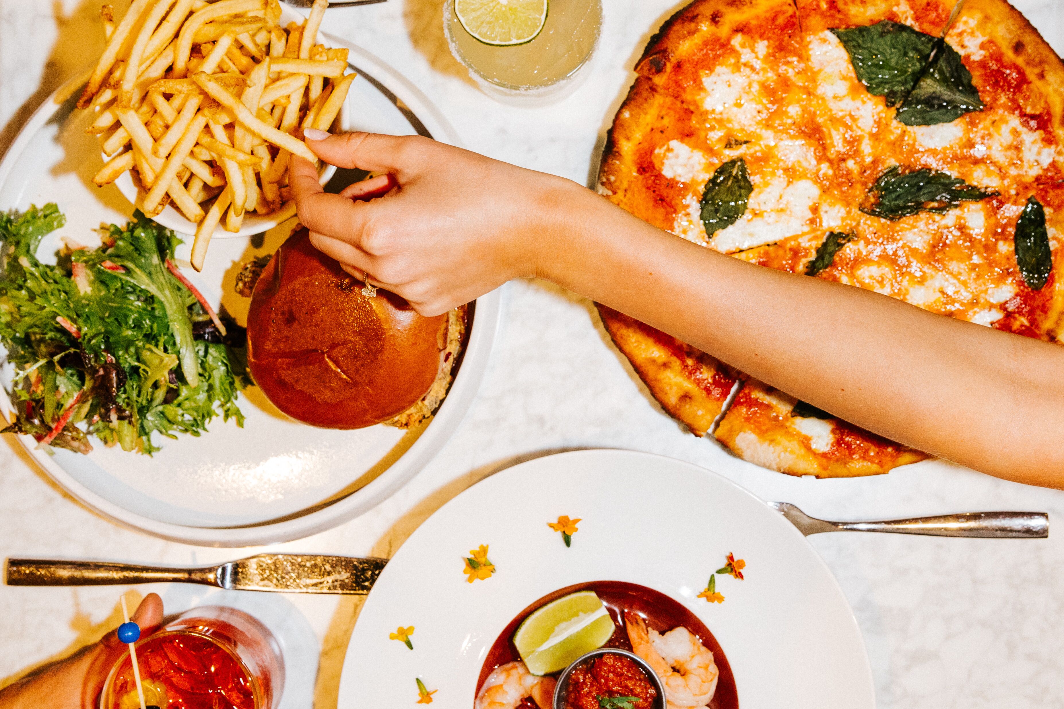 A table with a plate of fries, a burger, a pizza, and a salad.