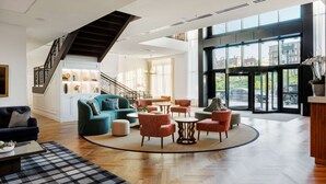 A spacious lobby with a staircase, modern furniture, and large windows offering city views. - Canopy By Hilton Boston Downtown (Boston)