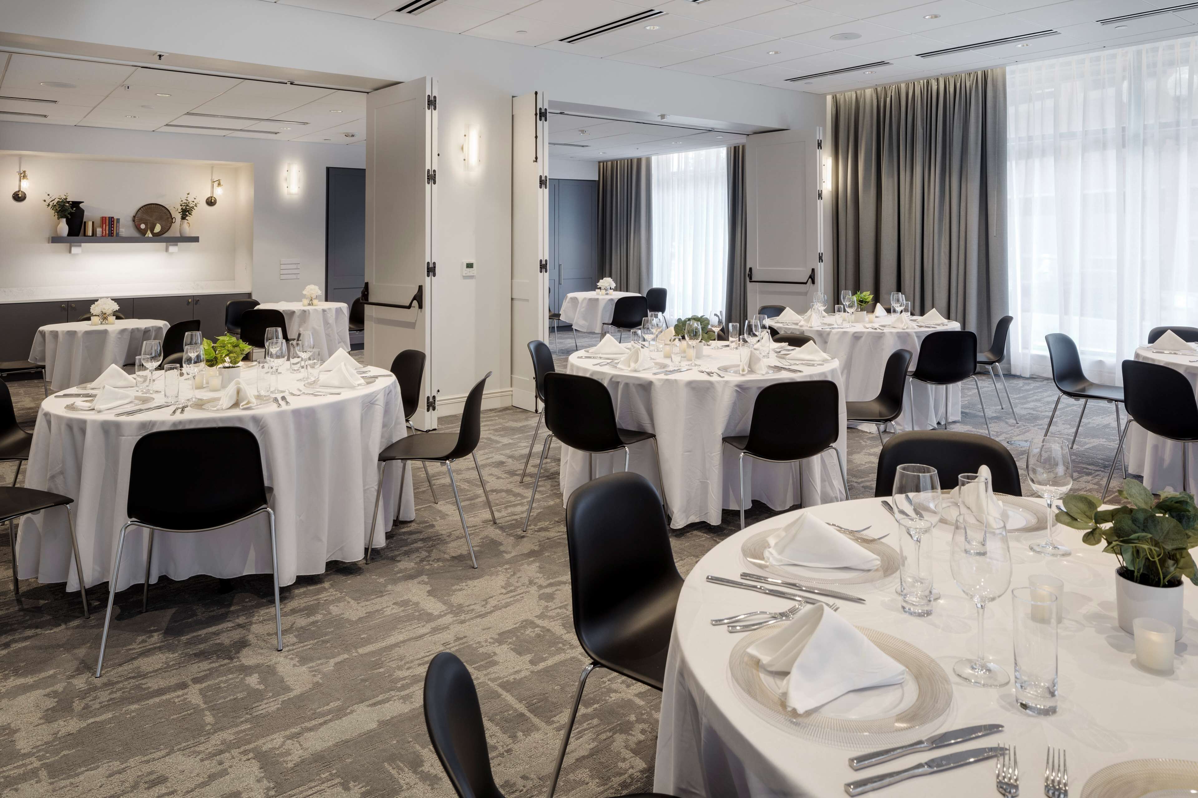 A conference room with round tables, black chairs, and white tablecloths.