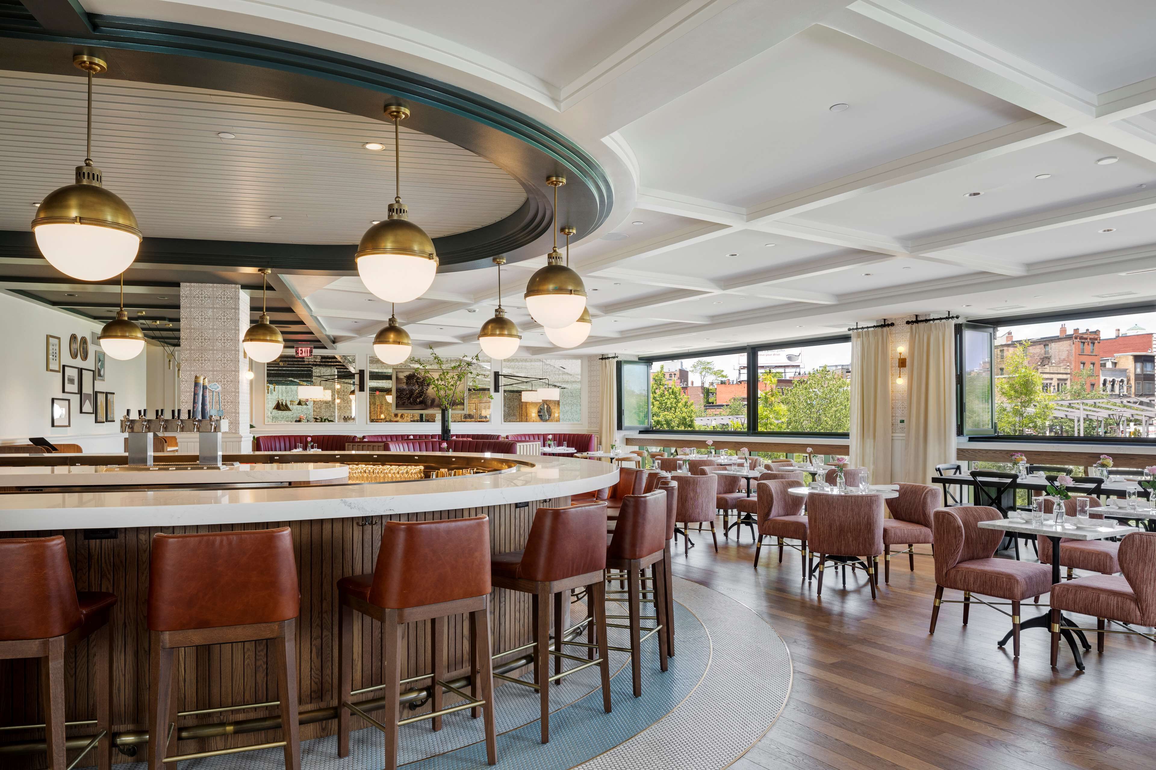 Un restaurante moderno con zona de bar, techos altos y grandes ventanales que ofrecen vistas del paisaje urbano.
