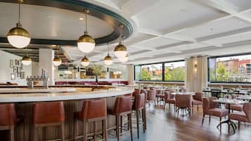 Un restaurante moderno con zona de bar, techos altos y grandes ventanales que ofrecen vistas del paisaje urbano.