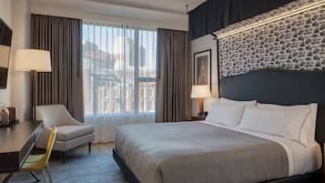 Une chambre d’hôtel avec un grand lit, un bureau avec une chaise, une fenêtre avec des rideaux et un mur décoré d’un motif.