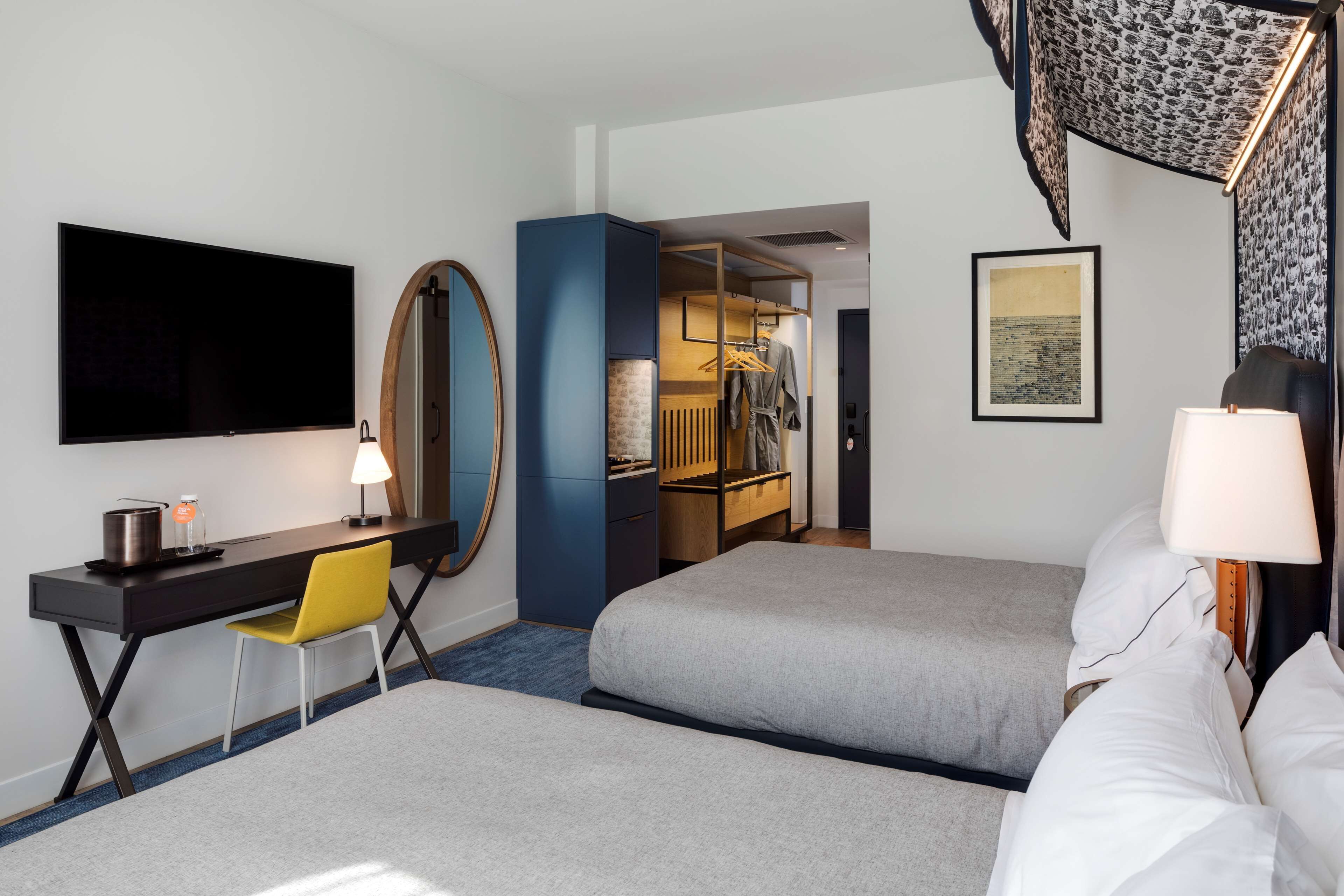 A hotel room with two beds, a desk with a chair, a TV, a mirror, and a wardrobe.