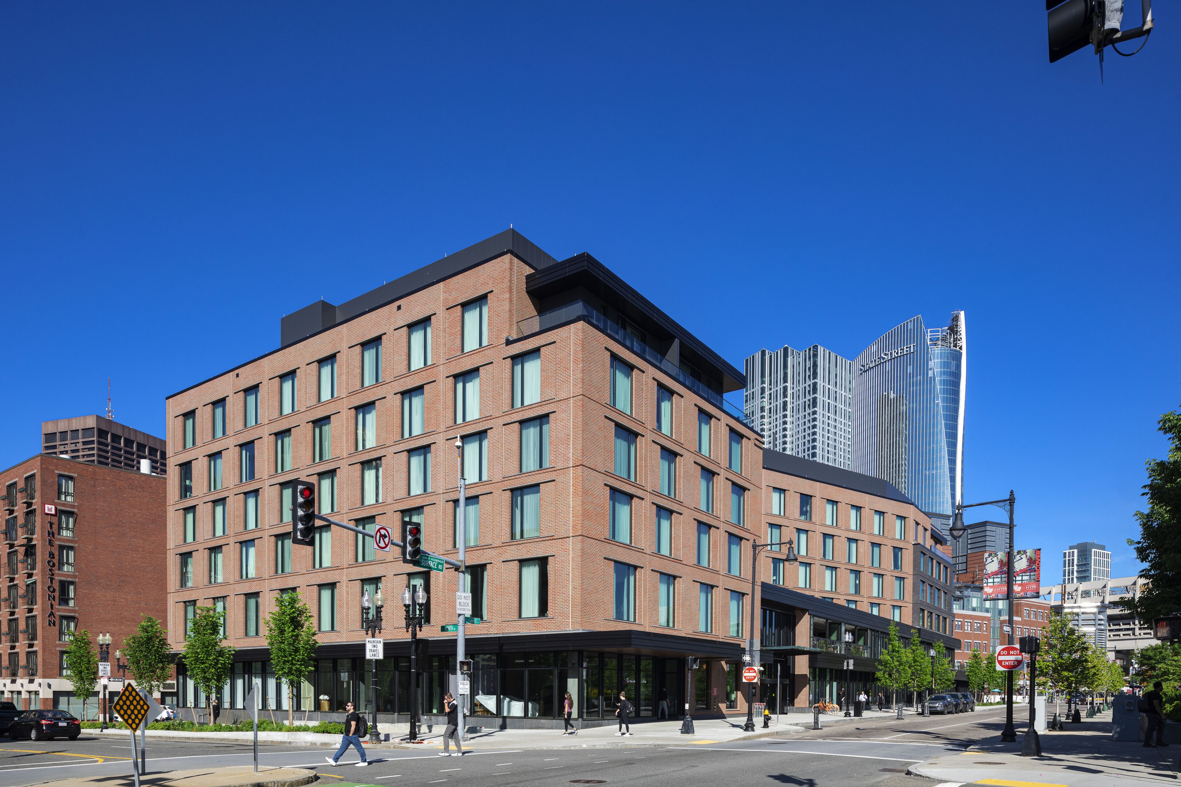 Un hotel de varios pisos con fachada de ladrillo moderno, ventanas amplias y ubicación en esquina en una intersección concurrida.